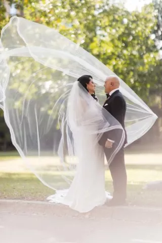 Bride and groom pose outside, the bride's veil catching on a dramatic wind