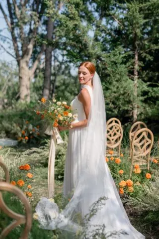 Model in simple bridal attire holding bouquet standing among the ceremony scene at Petal and Thorn Flower Farm