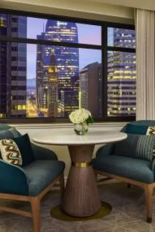 Cozy up in the stylish queen room sitting area at the Ritz-Carlton, Denver, showcasing plush teal chairs and a stunning cityscape view, perfect for a relaxing evening or intimate gathering