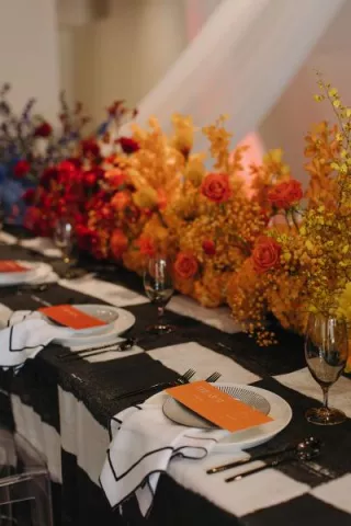 Maximalist tablescape featuring black and white checkered tablecloth and ombre rainbow florals