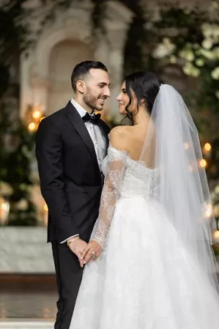 A gorgeous couple in classic wedding attire with long veil at elegant greenery altar with Armenian touches