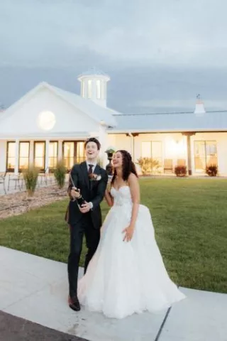 Bride and groom pop champagne in front of modern venue
