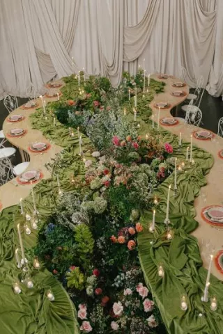 Serpentine tablescape featuring vivid décor, bright florals and romantic candlelight set against a draped background in editorial at The Woodland