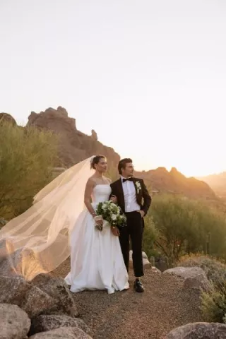 Bride and groom pose on the rocks of Camelback Mountain with the golden hour casting a glow behind them
