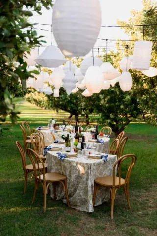 Serpentine table embrace an Italian aesthetic with paper lanterns hanging overhead in imagined backyard wedding on a private orchard