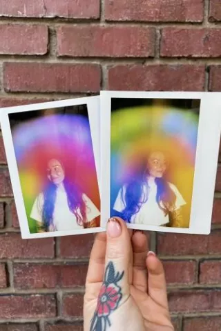Two physical aura photograph polaroids by Vivid violet Aura side by side against a brick wall