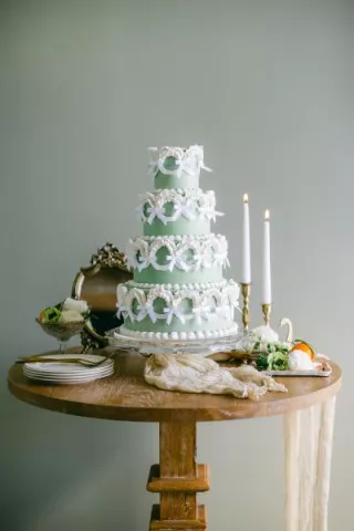 Four-tier green wedding cake in a vintage style with tiers lined with white bows