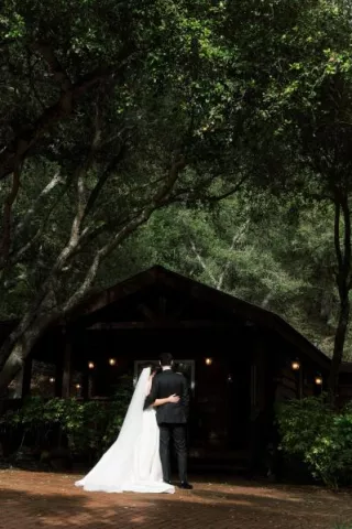 Bride and groom pose, shaded by dark trees on the grounds of Villa Loriana