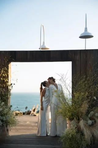 Couple shares a kiss in outdoor door frame, framed by yellow wildflowers and the sea in the background at The Sea Ranch Lodge