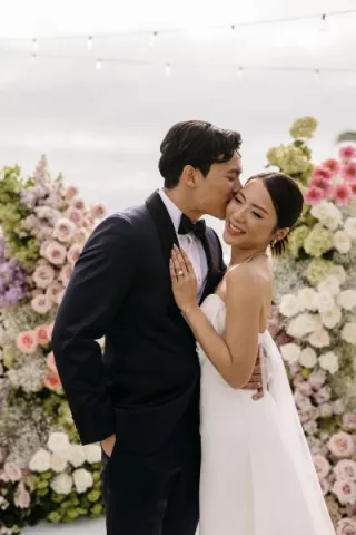 Groom kisses bride's cheek on lush altarspace platform on their wedding day at Montage Laguna Beach