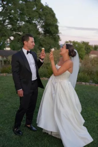 Bride and groom eat from ice cream cones on the ground of their outdoor wedding