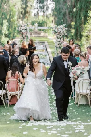 Samantha and Ryan cheer as they walk back down the floral-lined aisle at Sierra Madre