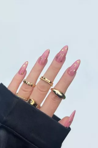 Hand peeking out of sweatshirt sleeve, with Deco Beauty nail sticker manicure and gold rings on fingers