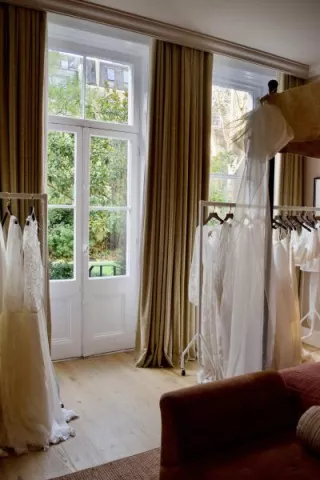Bridal gowns from E&W Couture displayed on garment racks inside a London suite during the New Archive collection launch, with natural light and garden views in the background.