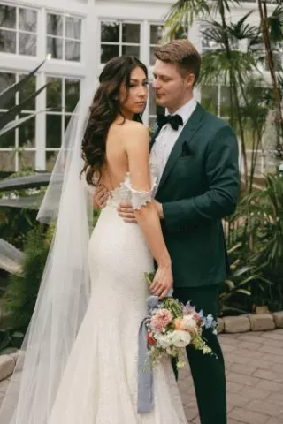 Hannah Fuchigami and Gunnar Conley pose at the W.W. Seymour Botanical Conservatory before their wedding, with lush greenery and floral accents in the background