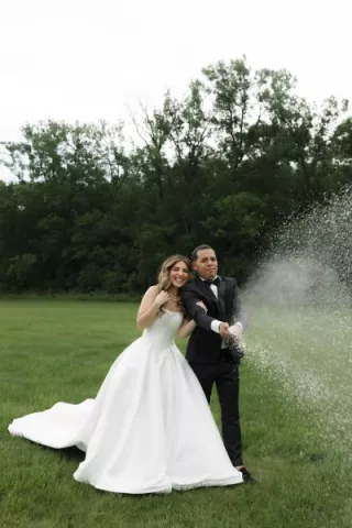 Bride and groom stand on lush grounds of Belle Âme Vineyard, sparying champagne to celebrate their wedding day