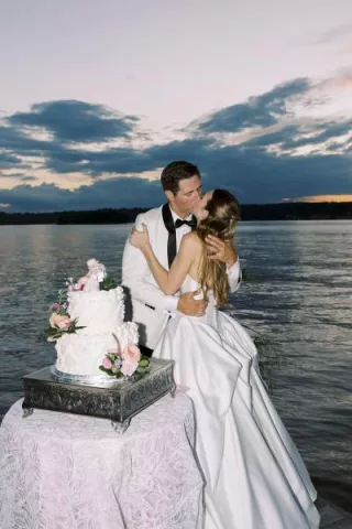 Bride and groom share a kiss during lakeside cake cutting as the sun sets on Pewaukee Lake