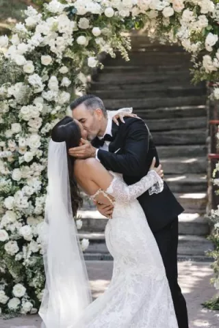 Bride and groom seal their vows with a kiss framed by an arch of lush white florals
