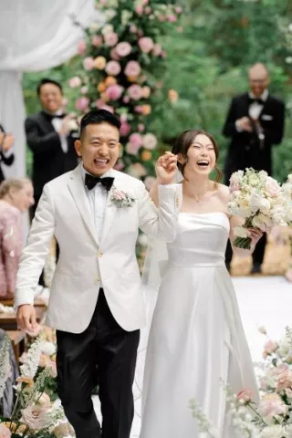 Bride and groom hold hands and cheer with joy while walking down aisle after outdoor wedding ceremony at Twin Willow Gardens