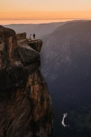 Bride and groom standing on the edge of Taft Point in Yosemite National Park at sunset, overlooking the expansive valley below with stunning cliffs in the background.