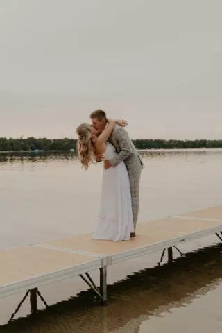 Bride and groom share kiss on a dock with lake in background in lakeside wedding day