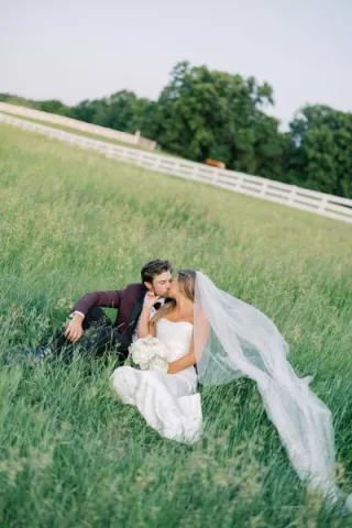 Bride and groom sit and share a kiss in a field on a private estate 