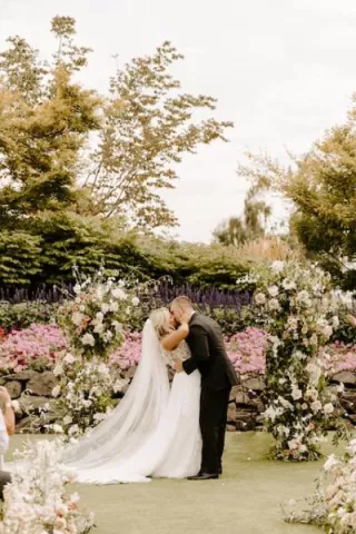 Kristin and Mason Share a Kiss in Front of Neutral Floral Arch After Exchanging Vows at Langdon Farms Golf Club