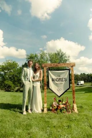 Sara and Billy stand by their custom made "Camp Andres" sign on their wedding day 
