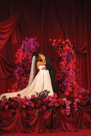 Bride and groom kiss at luxe altar featuring bright red and magenta floral installation and red draping backdrop at The Four Seasons Minneapolis