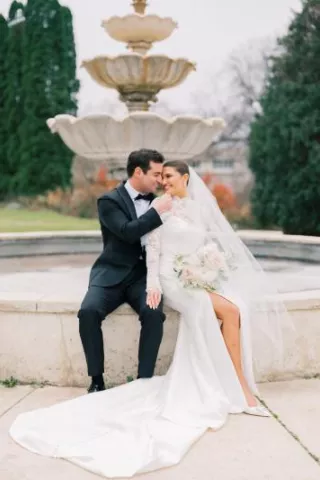 Bride and groom pose sitting at the edge of a water fountain 