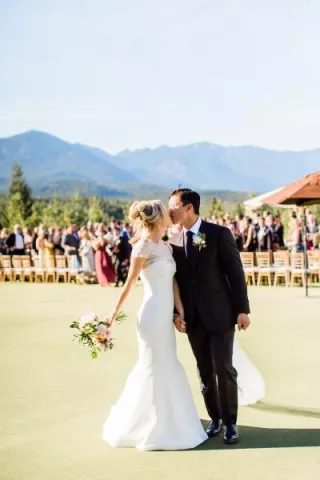 Bride and groom share a kiss after walking down the aisle in outdoor ceremony with mountainous backdrop at Tumble Creek