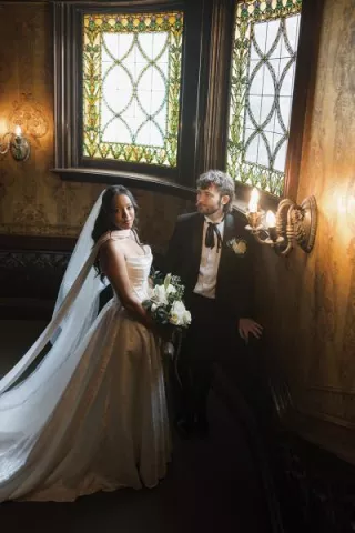 Bride and groom stand together framed by stained glass windows at Joslyn Castle