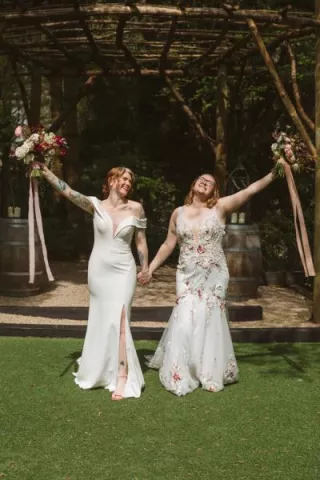 Two brides in different dresses and dark, autumnal bouquets smile after ceremony