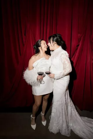 Models pose and share a kiss with drinks in hand in front of rich red draping