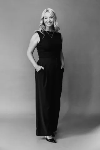 Headshot of Arizona Bride publisher Brittany O'Neill, standing wearing all black, smiling with hands in pockets
