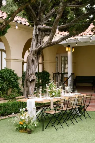 Table and chairs with nature-inspired decor and florals, underneath a large tree