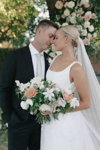 Bride and groom stand with foreheads pressed together, the bride holding her bouquet at their outdoor wedding day