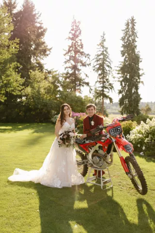 Bride with bouquet and groom in red suit pose with motocross dirt bike
