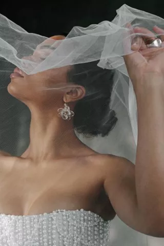 Model poses with holding veil over her face, showcasing stunning accessories in editorial shoot