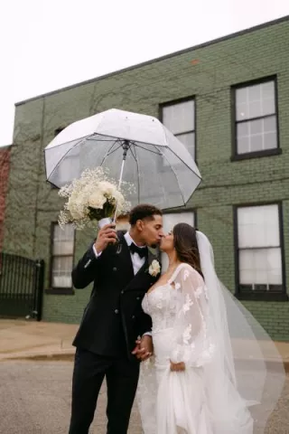 Bride and groom share a kiss under a clear umbrella outside of The Ivy House