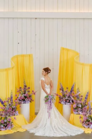 Model poses at altar with yellow fabric structures and lavender florals 