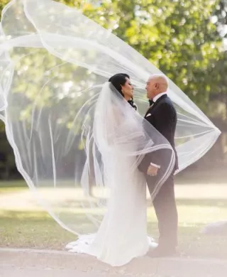 Bride and groom pose outside, the bride's veil catching on a dramatic wind