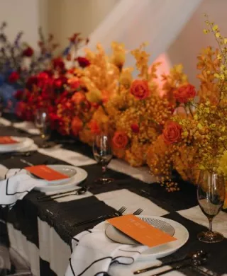 Maximalist tablescape featuring black and white checkered tablecloth and ombre rainbow florals