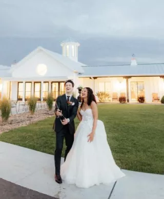 Bride and groom pop champagne in front of modern venue