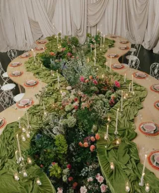 Serpentine tablescape featuring vivid décor, bright florals and romantic candlelight set against a draped background in editorial at The Woodland