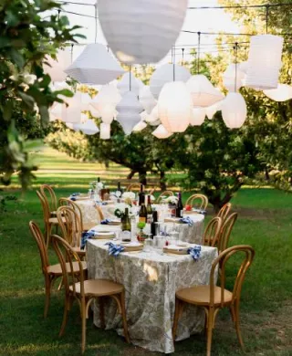 Serpentine table embrace an Italian aesthetic with paper lanterns hanging overhead in imagined backyard wedding on a private orchard