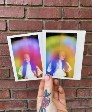 Two physical aura photograph polaroids by Vivid violet Aura side by side against a brick wall