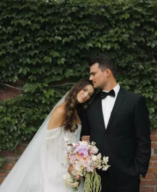Bride rests her head on groom's shoulder in front of an ivy backdrop at The Bohemian Gardens