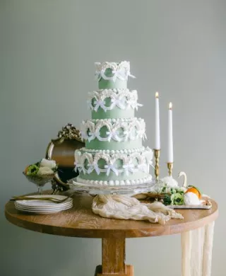 Four-tier green wedding cake in a vintage style with tiers lined with white bows