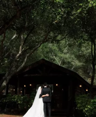 Bride and groom pose, shaded by dark trees on the grounds of Villa Loriana